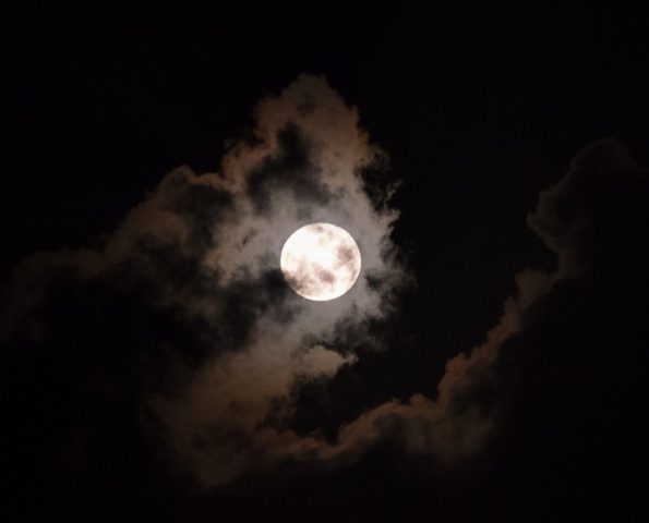 Full moon behind clouds glowing on a dark night sky