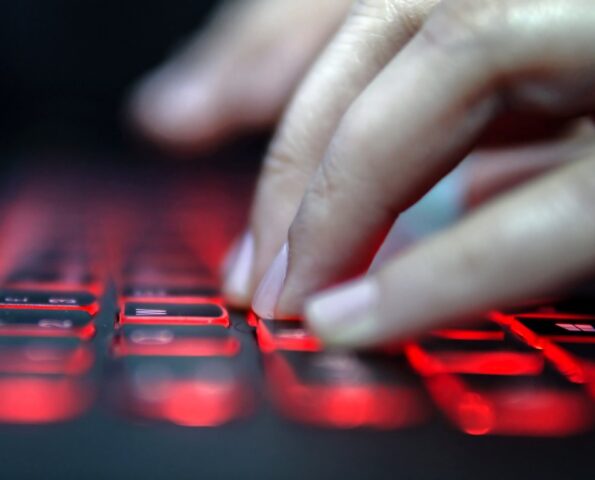 A hand typing at a keyboard that is backlit with red light