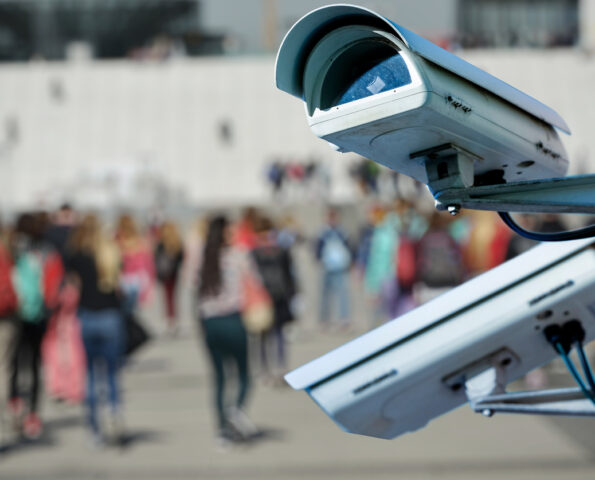 A picture of two security cameras with an out of focus crowd behind them.