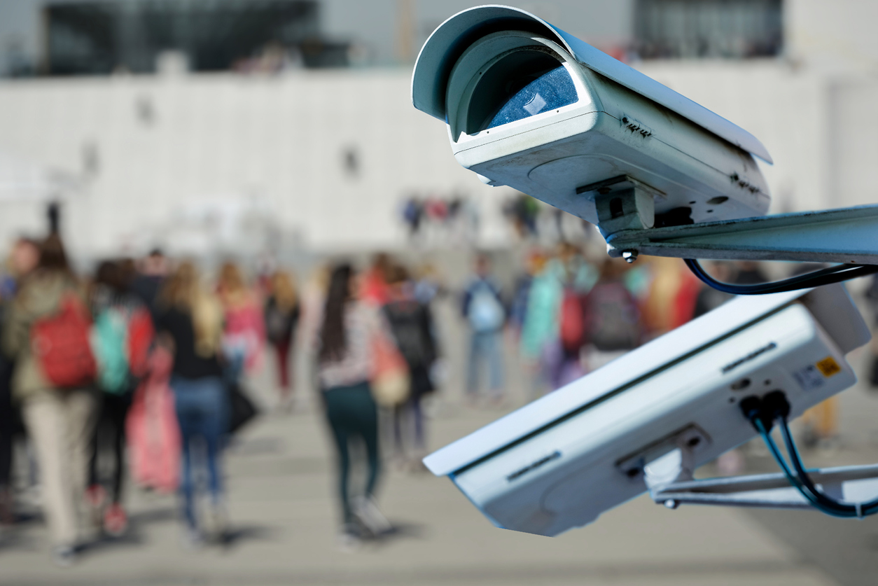 A picture of two security cameras with an out of focus crowd behind them.