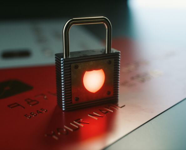 image of a padlock on top of a couple credit cards. In the center of the padlock is a symbol of a shield glowing red.