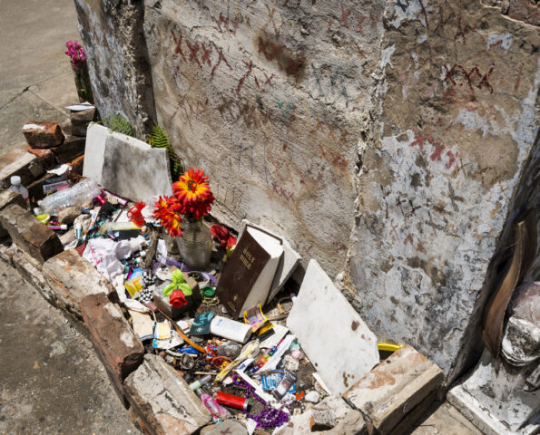 The tomb of Marie Laveau in New Orleans. It is a plaster crypt covered in multiple sets of handwritten Xs. There are offerings such as flowers and books and small objects.