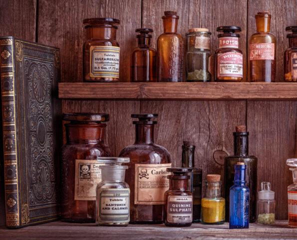 A wooden shelf with antique glass bottles. The bottles contain various medicines, poisons, and chemicals.