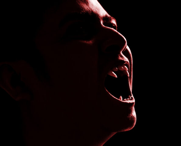 A shadowy vampire showing their fangs on a dark background