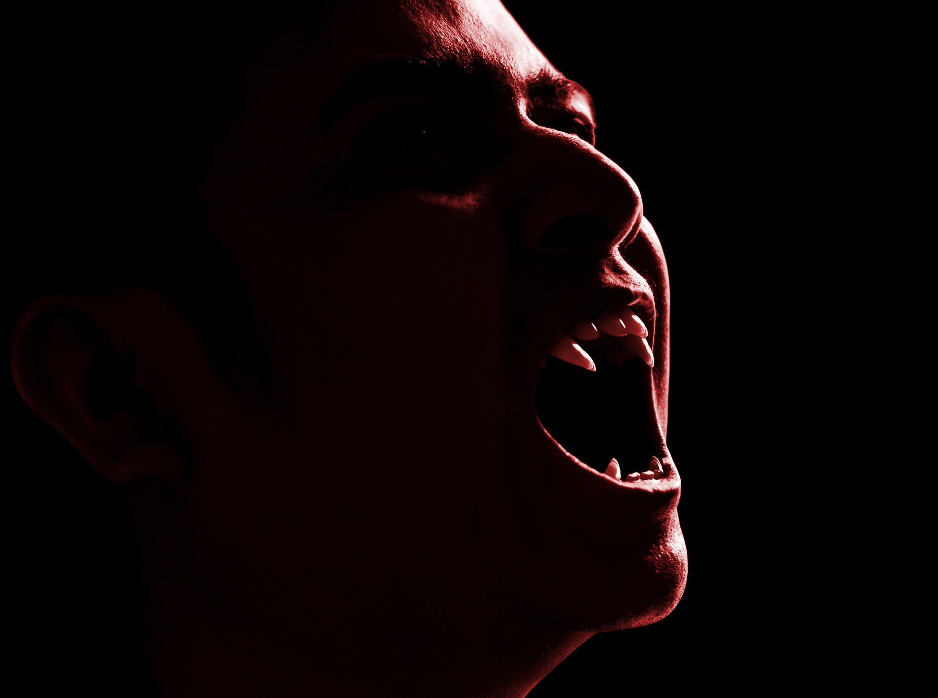 A shadowy vampire showing their fangs on a dark background