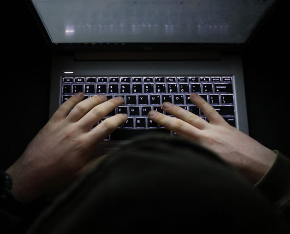 A top-down image of a person in a hoodie typing on an illuminated keyboard against a black background