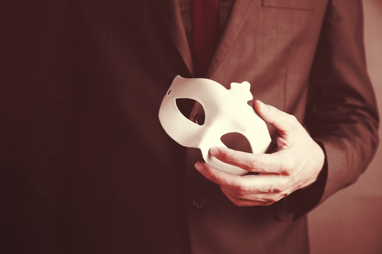 A man in a business suit holding a blank masquerade mask