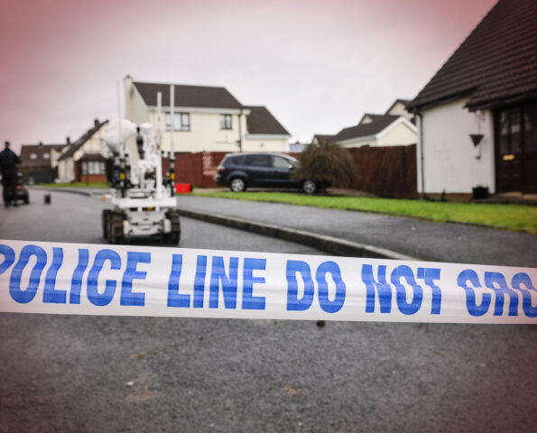 Police tape closes off a residential street as army ATOs use a robot to make safe a suspicious device